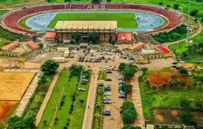 A lush green soccer pitch inside a large open-air stadium bowl structure.