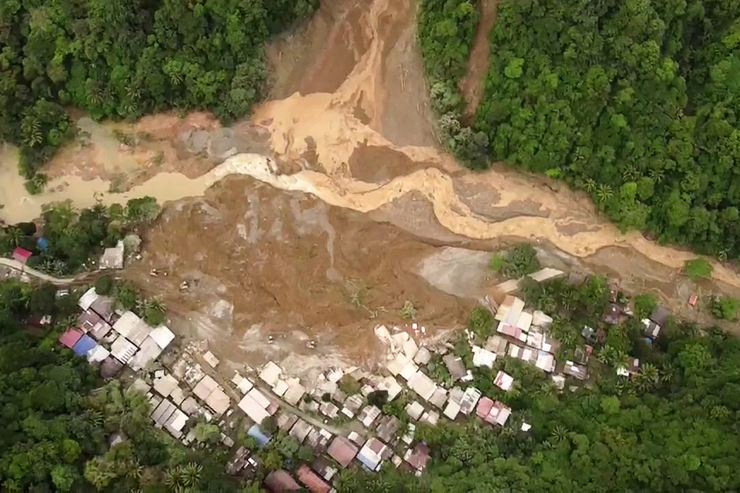 Aerial view of a landslide impacting a residential area near a forested slope.