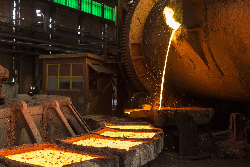 Molten metal being poured from a tilting furnace into molds inside a heavy industrial foundry.