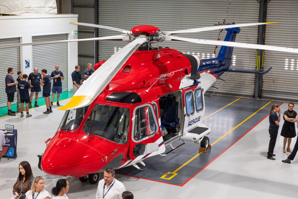 A rescue helicopter on display inside a hangar during an open day event with visitors.