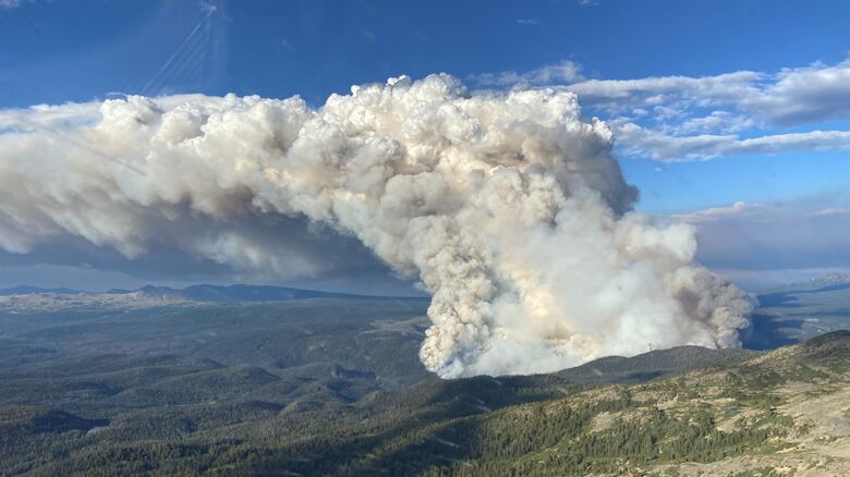 Thick smoke rising above forested hillsides during a severe regional wildfire.