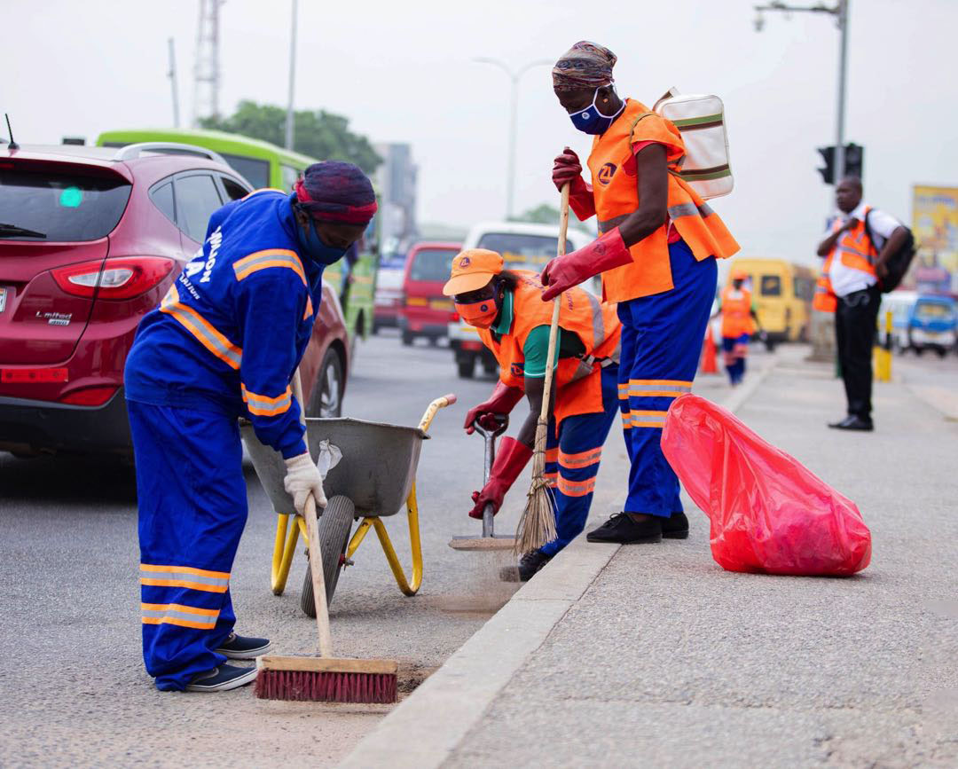 Sanitation workers sweeping and cleaning a roadside curb and street in Accra, Ghana.