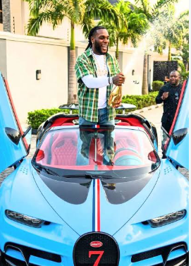 Burna Boy celebrating with champagne in front of his Bugatti Chiron