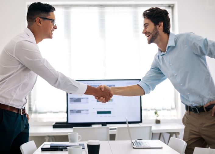 Business professionals shaking hands across a conference table in an office.