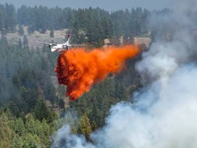 Firefighting aircraft dropping red fire retardant over a dense forest fire zone.
